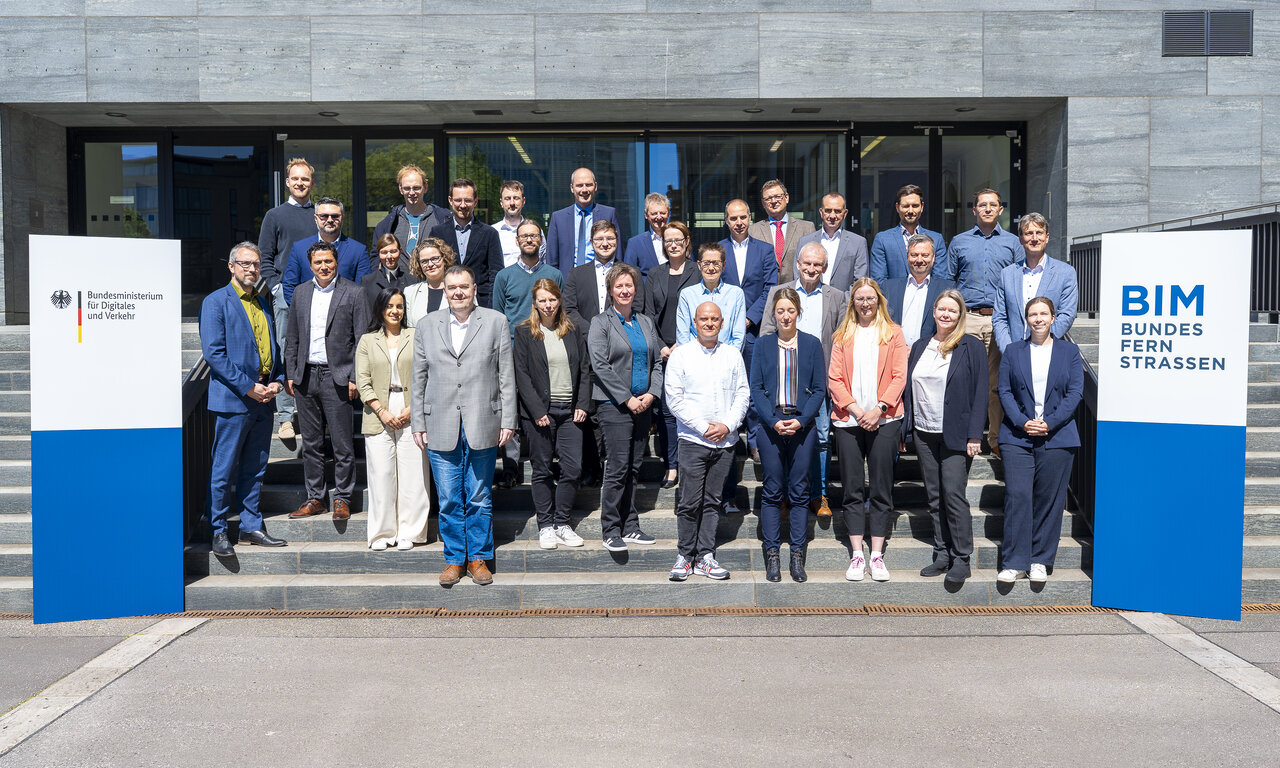 Gruppenfoto der Teilnehmenden der Bund-/Länder-Dienstbesprechung auf den Treppenstufen vor dem Bundesministerium für Verkehr, flankiert von zwei Aufstellern mit Logo des Ministeriums und BIM Bundesfernstraßen