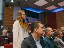 Eine Teilnehmerin aus dem Publikum hat das Mikrofon in der Hand und stellt eine Frage an das Podium