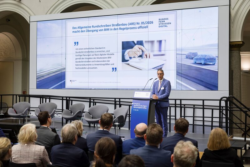 MDirig Steffen Müller, Leiter der Unterabteilung Straßen- und Ingenieurbau im Bundesministerium für Verkehr, beim Dialogforum Bundesfernstraßen Digital am 26. März 2026, im Hintergrund: Präsentationsfolie zum Allgemeinen Rundschreiben Straßenbau Nr. 05/2026