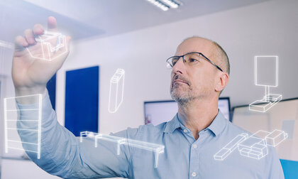 Ein Planer verschiebt symbolhaft vor einer Glaswand Objekte von der realen in die digitale Welt.