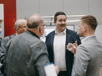 Teilnehmende beim Gespräch während der Kaffeepause, vier Männer in grauen und blauen Anzügen