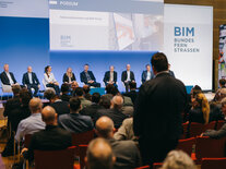 Mann aus dem Publikum steht und spricht ims Mikrofon, im Hintergrund das Podium "Rahmendokumente und BIM-Portal"