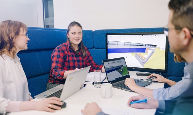 Vier Personen besprechen an einem Tisch ein 3D-Modell auf Monitor und Laptops