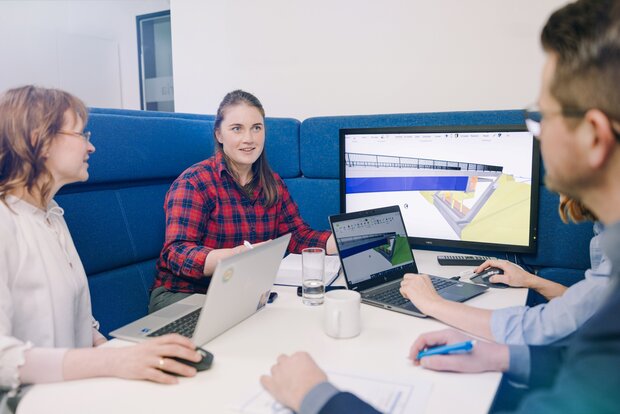 Vier Personen besprechen an einem Tisch ein 3D-Modell auf Monitor und Laptops