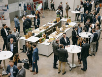 Blick von oben auf die Teilnehmenden des FAchsymposiums während einer Kaffeepausen, Menschen verteilt an Stehtischen im Gespräch, in der Mitte ein Buffet