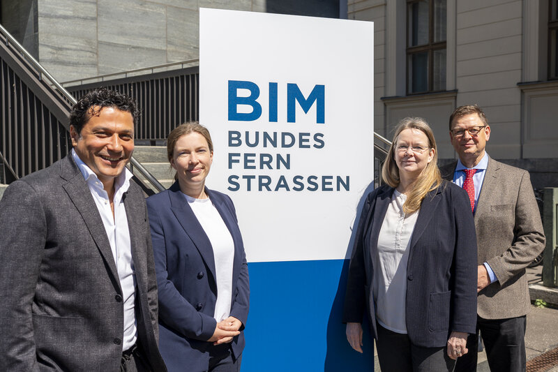 Vier Teilnehmende der Bund-/Länder-Dienstbesprechung vor dem Aufsteller mit Schriftzug "BIM Bundesfernstraßen"