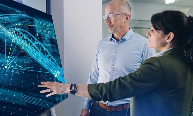 Ein Mann und eine Frau deuten auf einen Bildschirm mit einem digitalen Bauwerksmodell