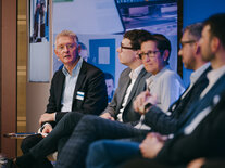 Der Moderator stellt eine Frage an die Panel-Teilnehmenden