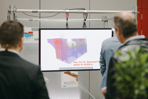 Zwei Personen stehen diskutierend vor einem Bildschirm, auf dem ein BIM-Modell zu erkennen ist