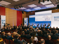 Gut gefüllter Saal vor Ort, das zahlreiche Publikum blickt auf die Bühne zu den Panel-Diskutanten