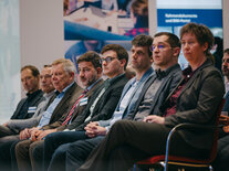 Acht Teilnehmende im Publikum sitzen in einer Reihe