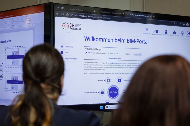 Zwei Teilnehmerinnen des Dialogforums Bundesfernstraßen Digital im März 2026 blicken an einer Themeninsel auf einen Bildschirm, der die Startseite des BIM-Portals zeigt.