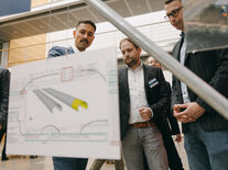 Drei Teilnehmende diskutieren vor einer Plandarstellung