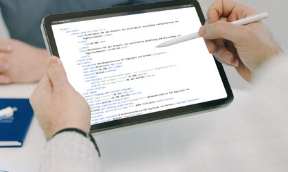 Eine Hand hält einen Tablet-Computer. Auf dem Bildschirm sind technische Code-Zeilen zu sehen, die die Transformation von Richtlinien in Smarte Standards darstellen.