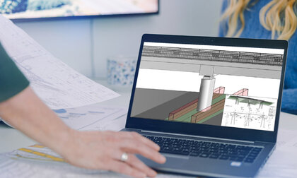 Ein Laptop steht auf einem Schreibtisch. Auf dem aufgeklappten Bildschirm ist ein BIM-Modell zu erkennen. Im Vordergrund ist die Hand einer Bearbeiterin zu sehen, die mit dem Touchpad navigiert.