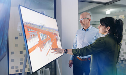 Ein Mann und ein Frau stehen vor einem Großbilschirm, die Frau deutet auf die BIM-Visualisierung eines Brückenbauwerks