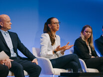 Eine Teilnehmende auf dem Podium spricht und untermalt ihren Beitrag mit Handgesten