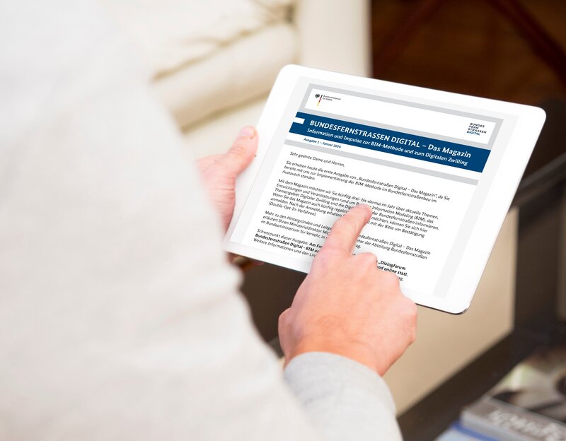 Person hält ein Tablet-Computer in den Händen und liest auf diesem den Newsletter "Bundesfernstraßen Digital - Das Magazin"